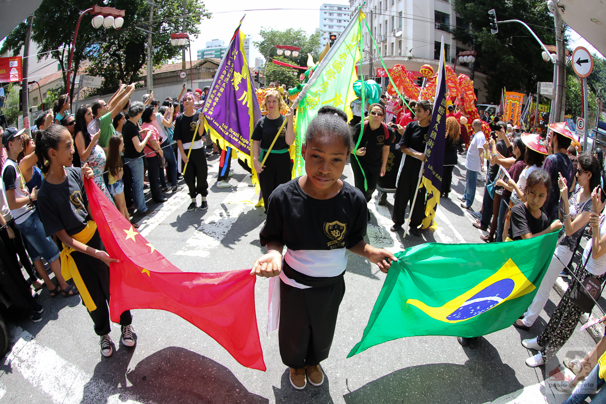 Participantes en la celebración del Año Nuevo Chino de 2017 en São Paulo sostienen las banderas de China y Brasil, con una comparsa y público al fondo.